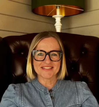 IMG_0430 Louise, counsellor in in Bournemouth, Poole and Christchurch, Dorset and Online smiling wearing glasses beneath a warm pendant light.